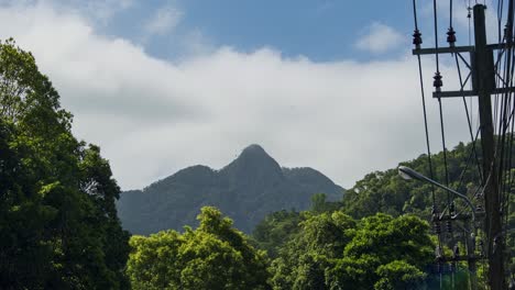 4K-Timelapse-of-Mountainous-Summit-with-Clouds-Forming-Over-the-Peak-against-a-Blue-Sky-on-the-Island-of-Koh-Chang-in-Thailand-with-Utility-Electrical-Poles-on-the-Side-of-the-Road