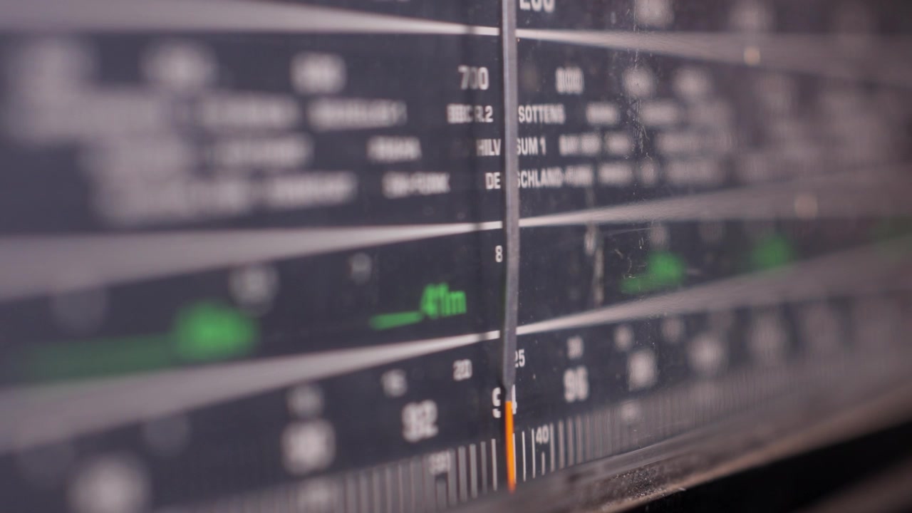 Vintage analog radiotuningskala med frekvenser og stationsnavne, makronærbillede mens drejeknappen finder det korrekte signal