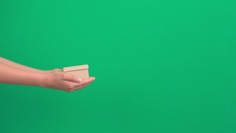 hands stretching out and giving small gift box over green screen chroma key background