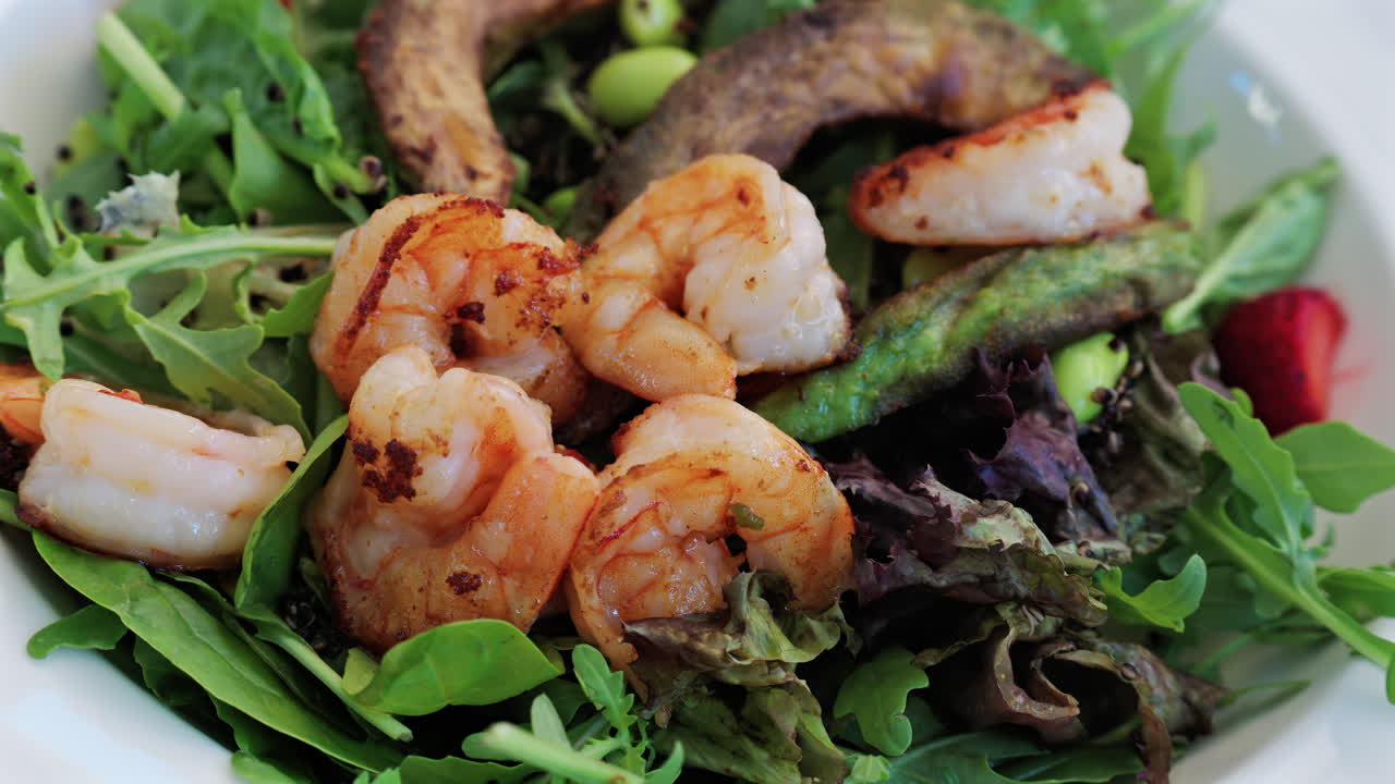 Close up of a fresh salad topped with grilled shrimp, leafy greens, avocado, and vegetables, perfect for healthy eating
