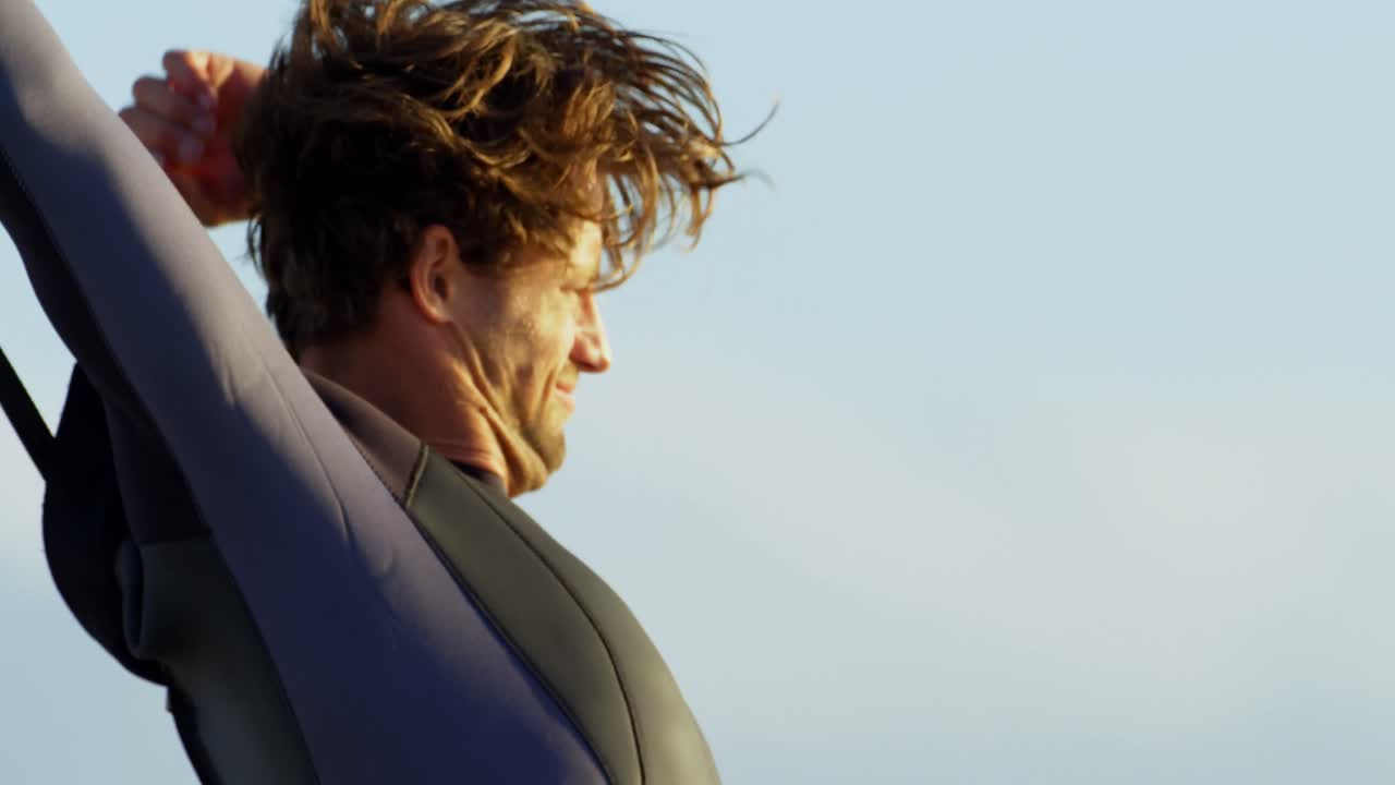 남성 서퍼가 해변 4k에서 웨이트 슈트를 입고 있습니다.