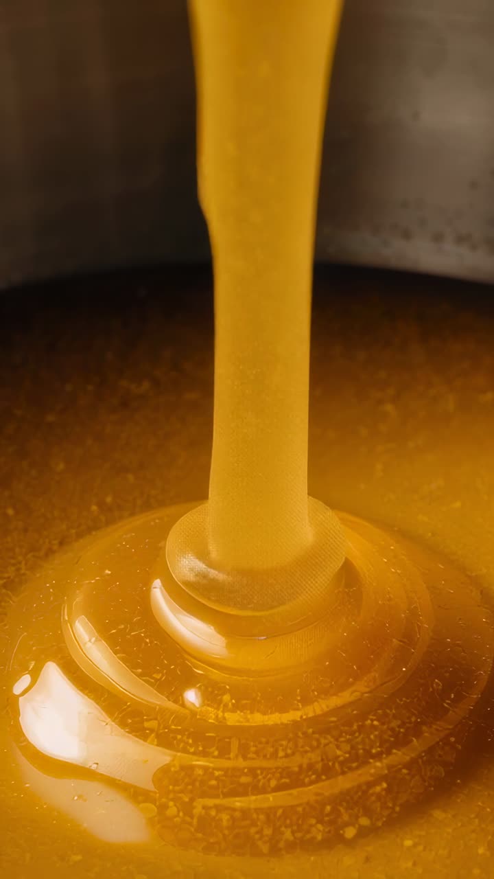 Video verticale: miele versato dal beccuccio superiore, flusso che forma anelli, che riempie una padella da cucina con macchie