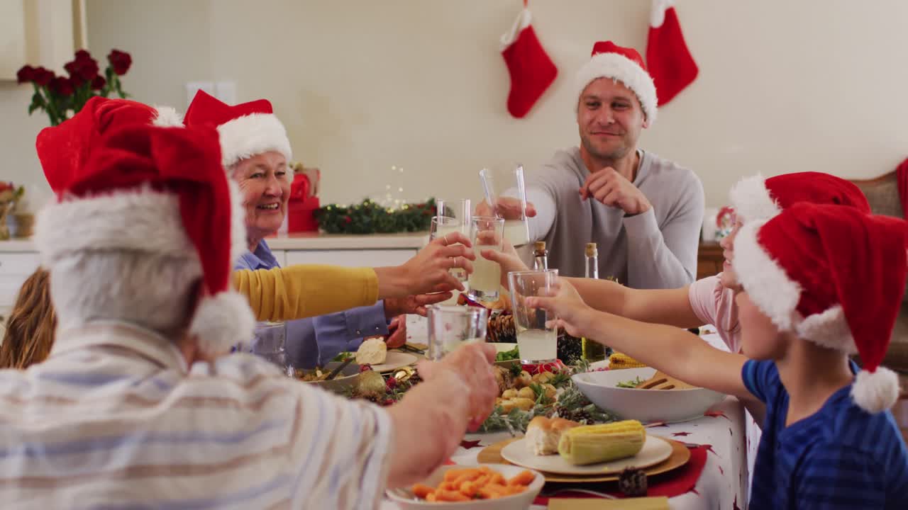 familia caucásica en sombreros de santa tostando y disfrutando del almuerzo juntos mientras están sentados en la mesa de comedor en