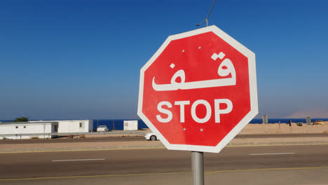 Stop-Sign-with-Arabic-Letters-in-front-of-a-Highway-Intersection-in-Jordan-with-Cars-Driving-in-Background