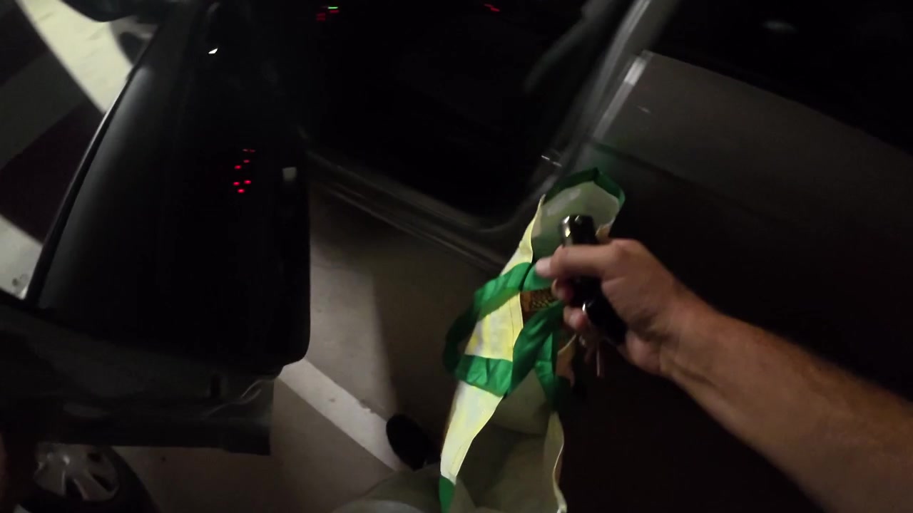Pessoa destrancando o carro e colocando sacola de compras no banco do passageiro.