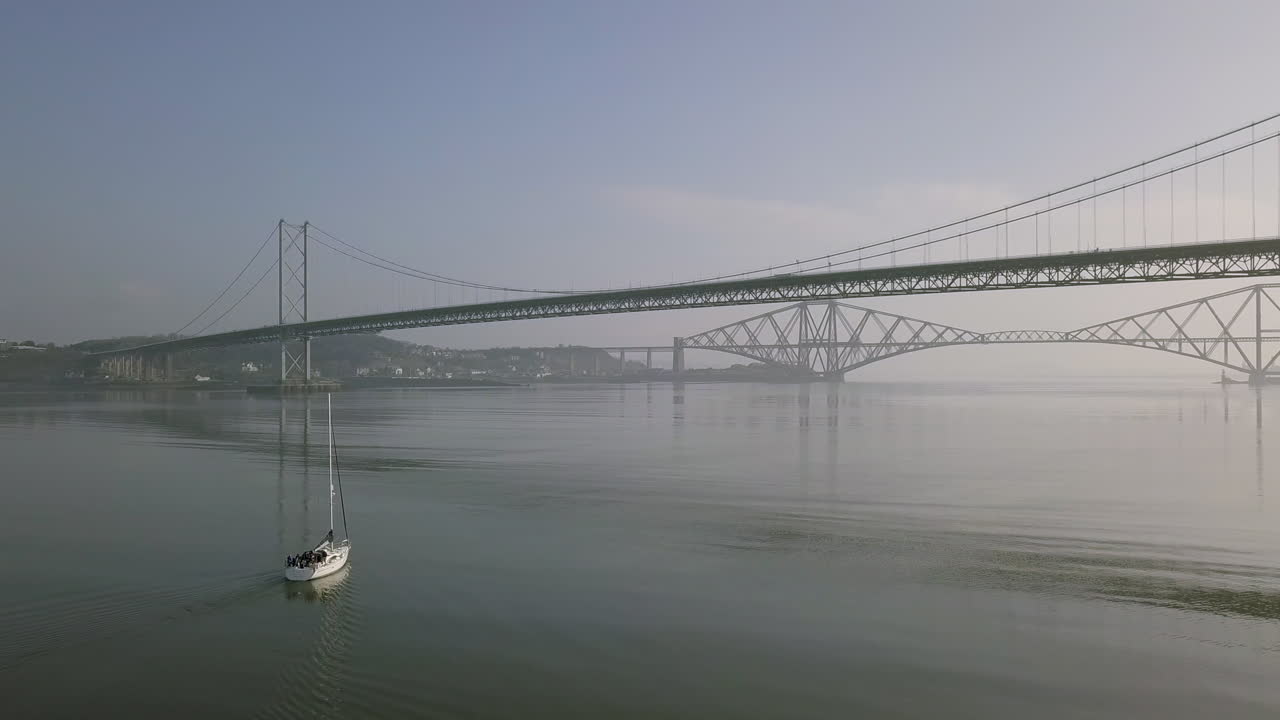 스코틀랜드 서부 로디안의 화창한 날 사우스 퀸스페리의 오래된 네 번째 도로 다리 아래를 여행하는 범선의 항공 영상