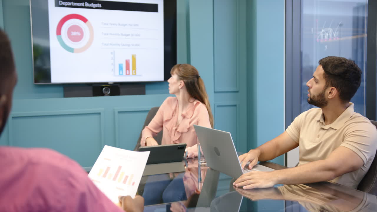 Presenting budget data, woman pointing at screen while diverse colleagues listen attentively
