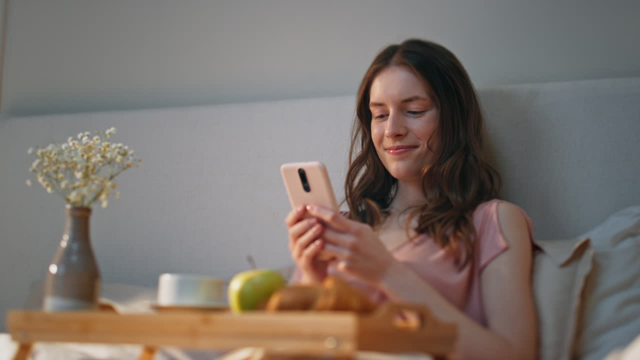 chica de la mañana usando teléfono inteligente en casa de cerca. sonriente mujer serena soñando