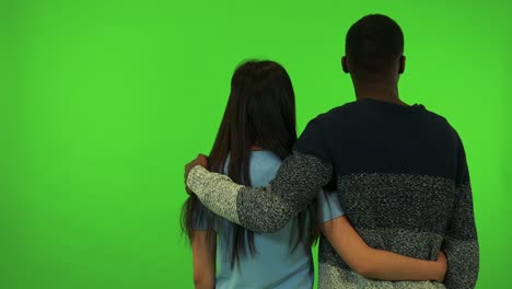 an asian woman and a black man watch something with their arms around each other and their backs to the camera - green screen studio