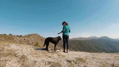 Chica-De-Pie-En-Una-Montaña-Con-Perro-Labrador-Negro,-En-Un-Soleado-Día-De-Otoño