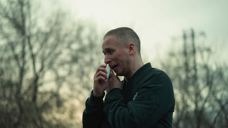 a close view of a man using a white inhaler, with background of trees, and sky in view