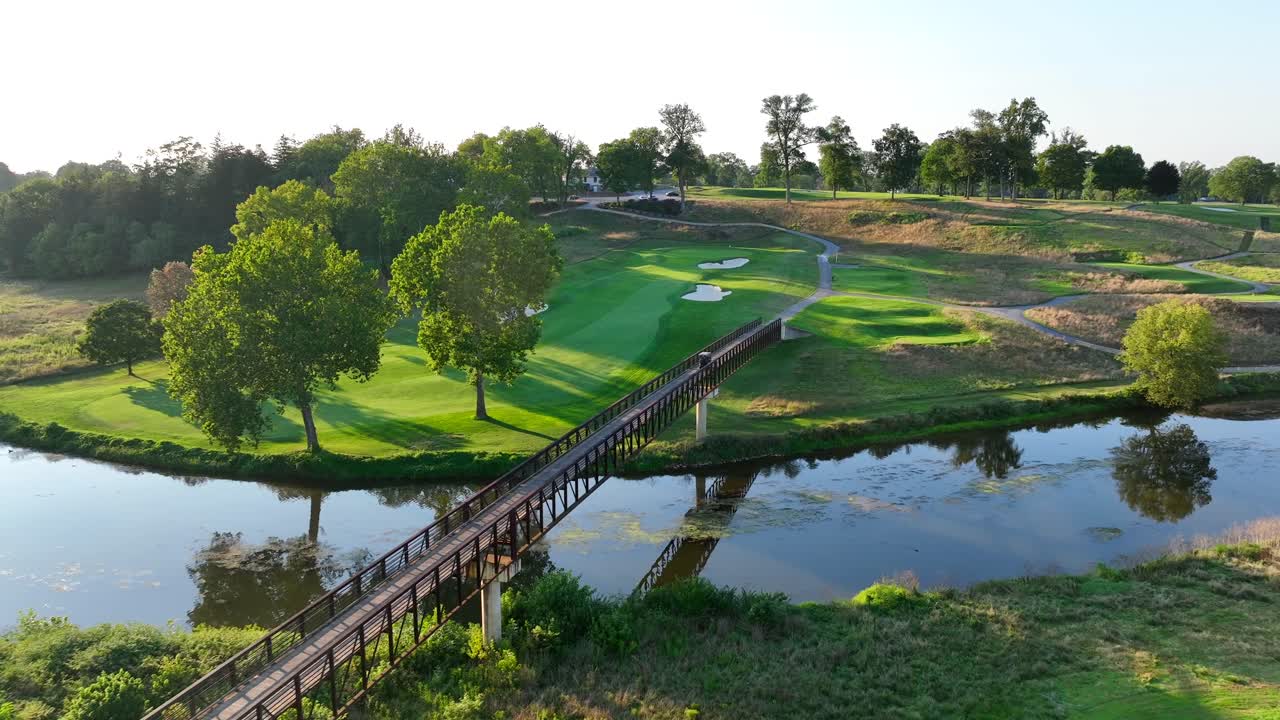 미국 의  ⁇ 빛 에 빛나는 골프 코스, 평화로운 강 을 가로지르는 나무 다리, 인접 한 초록색 페어웨이, 그리고 성숙 한 나무 들