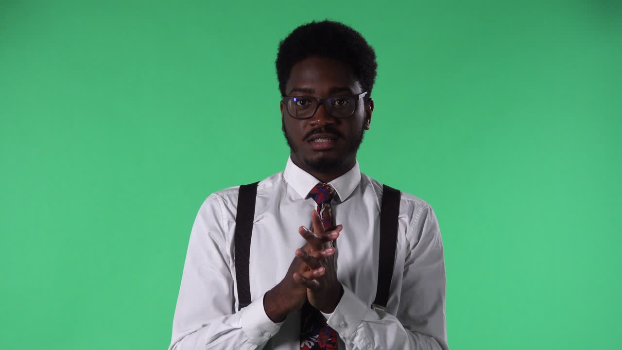 Portrait of young African American man reporting of interesting information and gesturing with his hands. Black male with tie and glasses in white shirt posing on green screen in studio. Close up