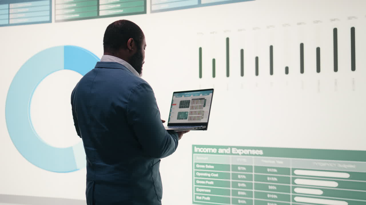 African American Businessman Analyzing Financial Data on Laptop and Large Screen