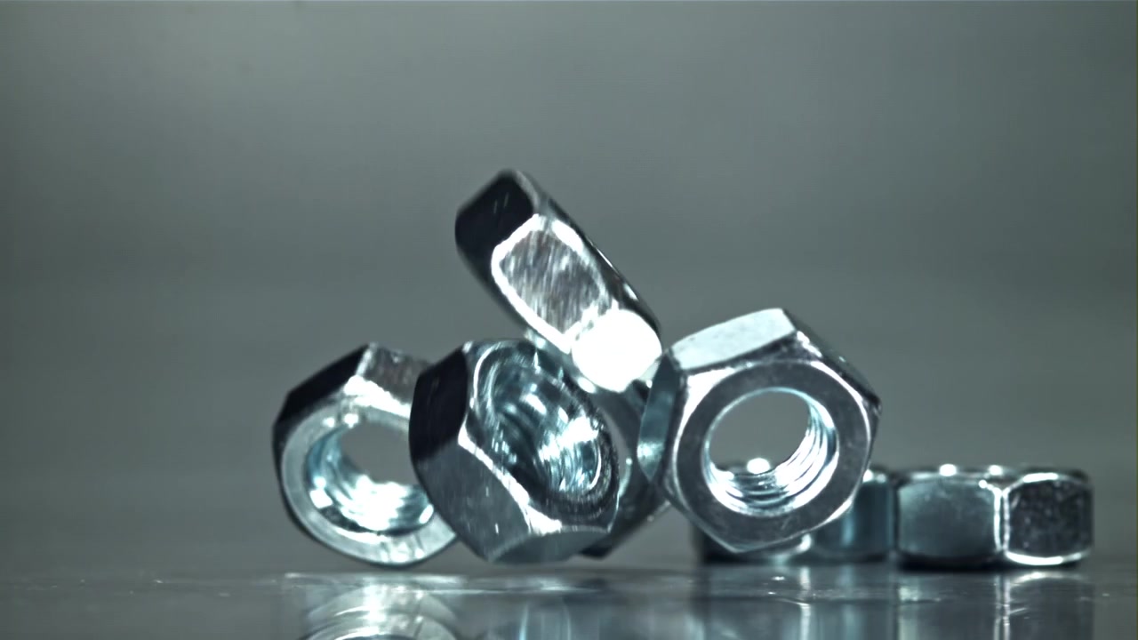 Metallmuttrar som faller i slow motion på en reflekterande yta.