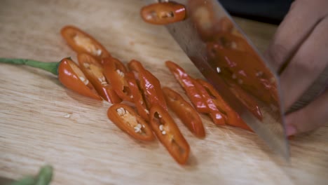 cutting a red chili pepper into slices with knife on wooden chopping board - close up