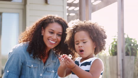 young mixed race mother and daughter blowing bubbles outside