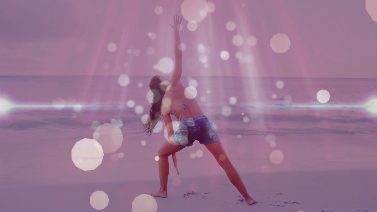 Woman shifting weight into right lunge doing fitness on sand with pink bokeh sweeping across body