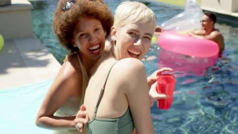 portrait of happy diverse friends with inflatables and drinking drinks at pool party in summer