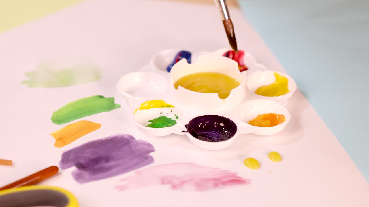 Artist hand mixes vibrant watercolor paints on palette, applying colors to paper under soft lighting