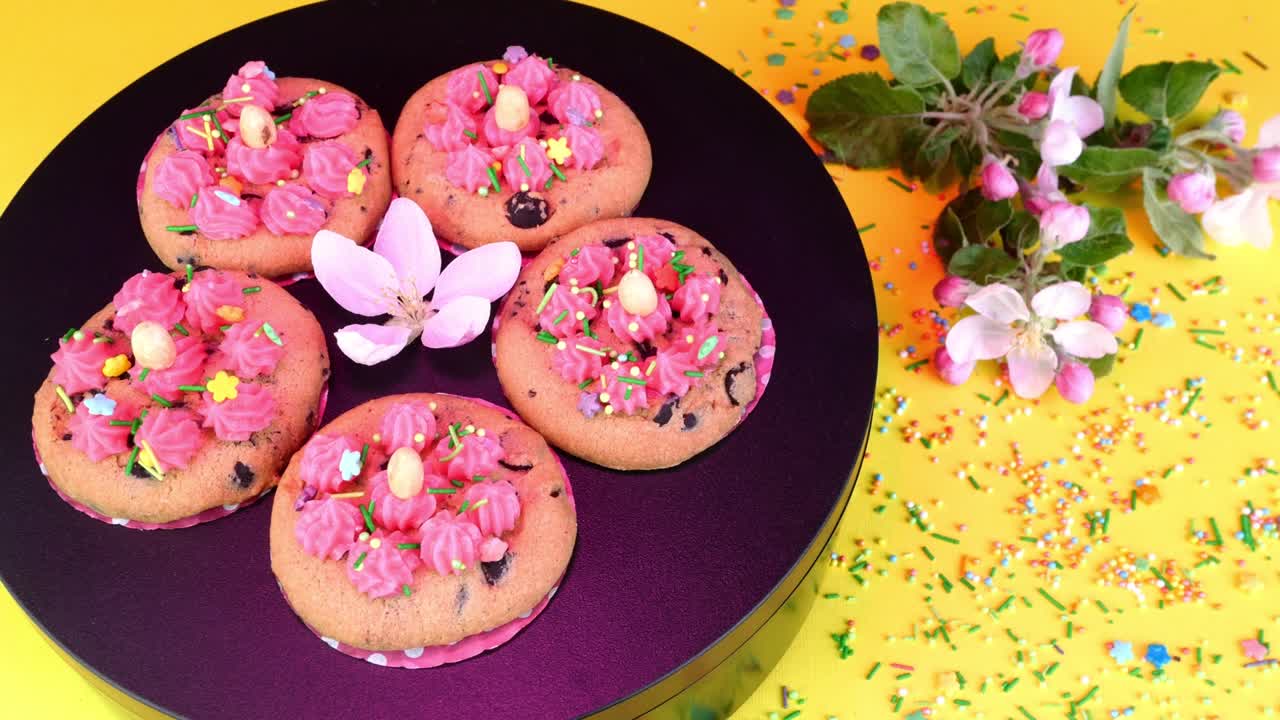 Biscuit décoré de crème vanille tournant lentement sur un plateau noir sous lumière rose. Friandises et desserts faits maison.