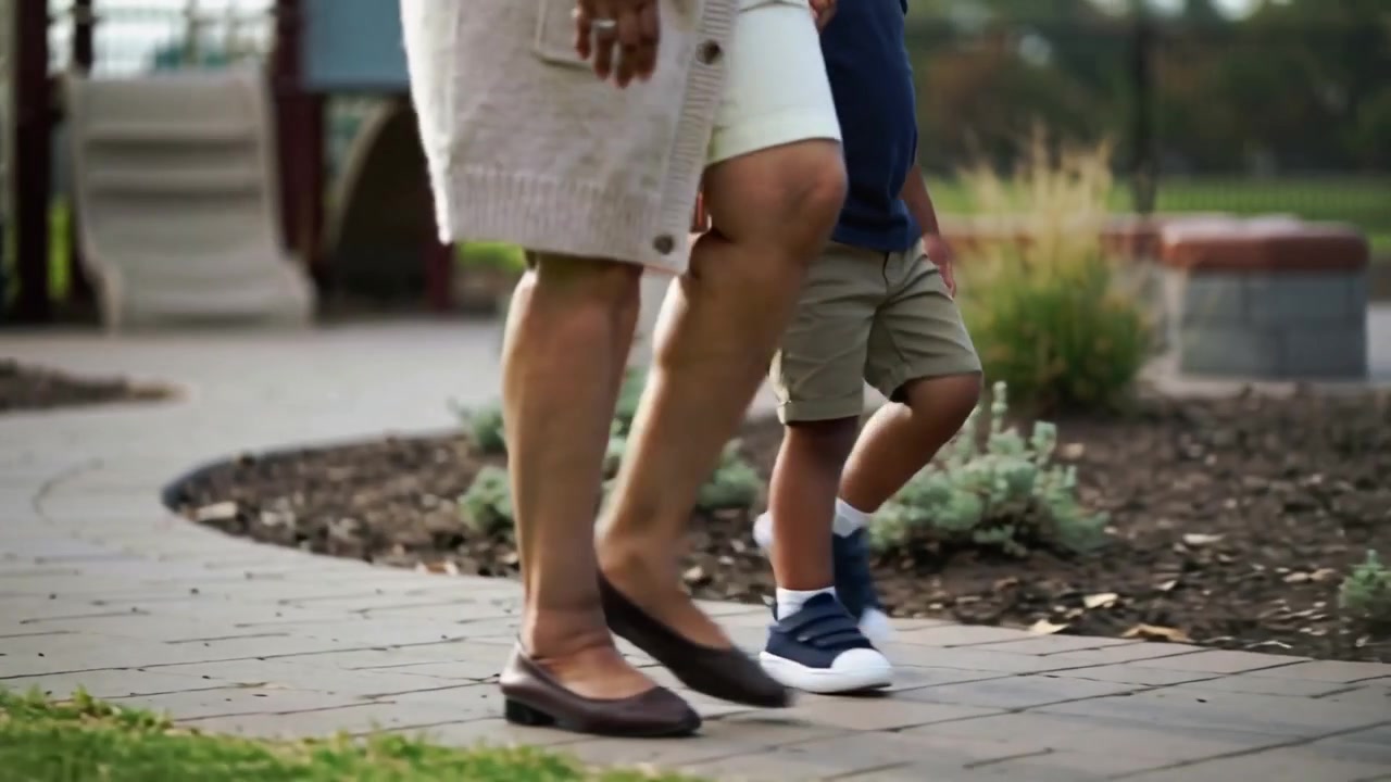 Stepping onto pavers, caregiver in skirt guiding and steadying child along park path for safety
