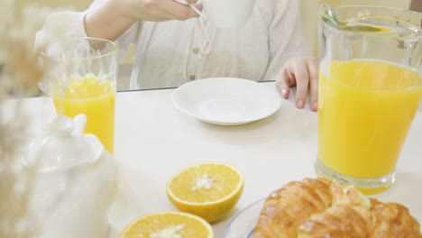 Woman-drinking-her-cup-of-coffee-with-fresh-orange-juice-and-croissant-on-breakfast-table