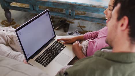 mixed race couple having a video call on laptop with copy space on the couch at vacation home