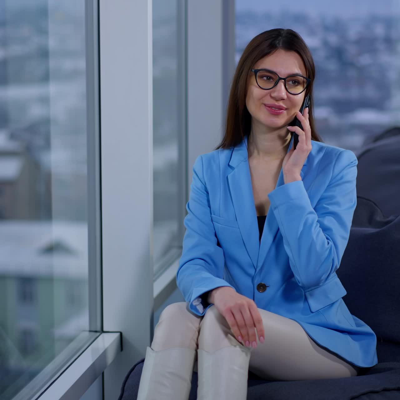 Good-looking lady having phone conversation. Woman in blue jacket speaks on the phone sitting at the window