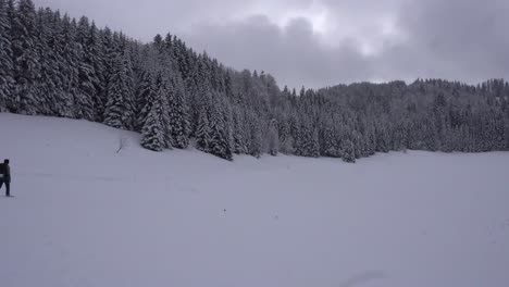 Man-Walking-in-the-Snow-in-the-French-Alps-during-a-Snowfall-with-a-Pine-Tree-Forest-in-the-Background