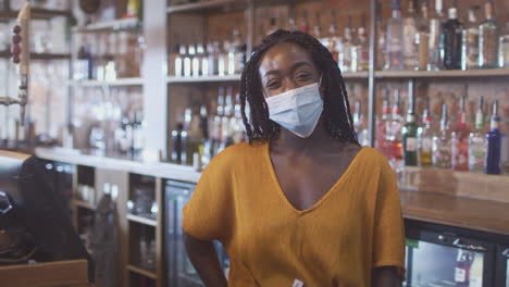 Portrait-Of-Female-Bar-Worker-Wearing-Face-Mask-During-Health-Pandemic-Standing-Behind-Counter