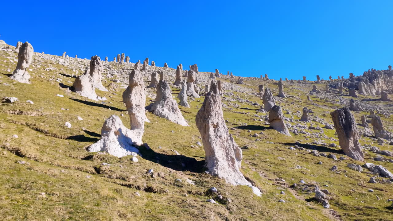 Pinnacoli di calcare su un fianco di collina erboso, baciati da un cielo azzurro limpido, con torri di tufo sparse che emergono dal verde.
