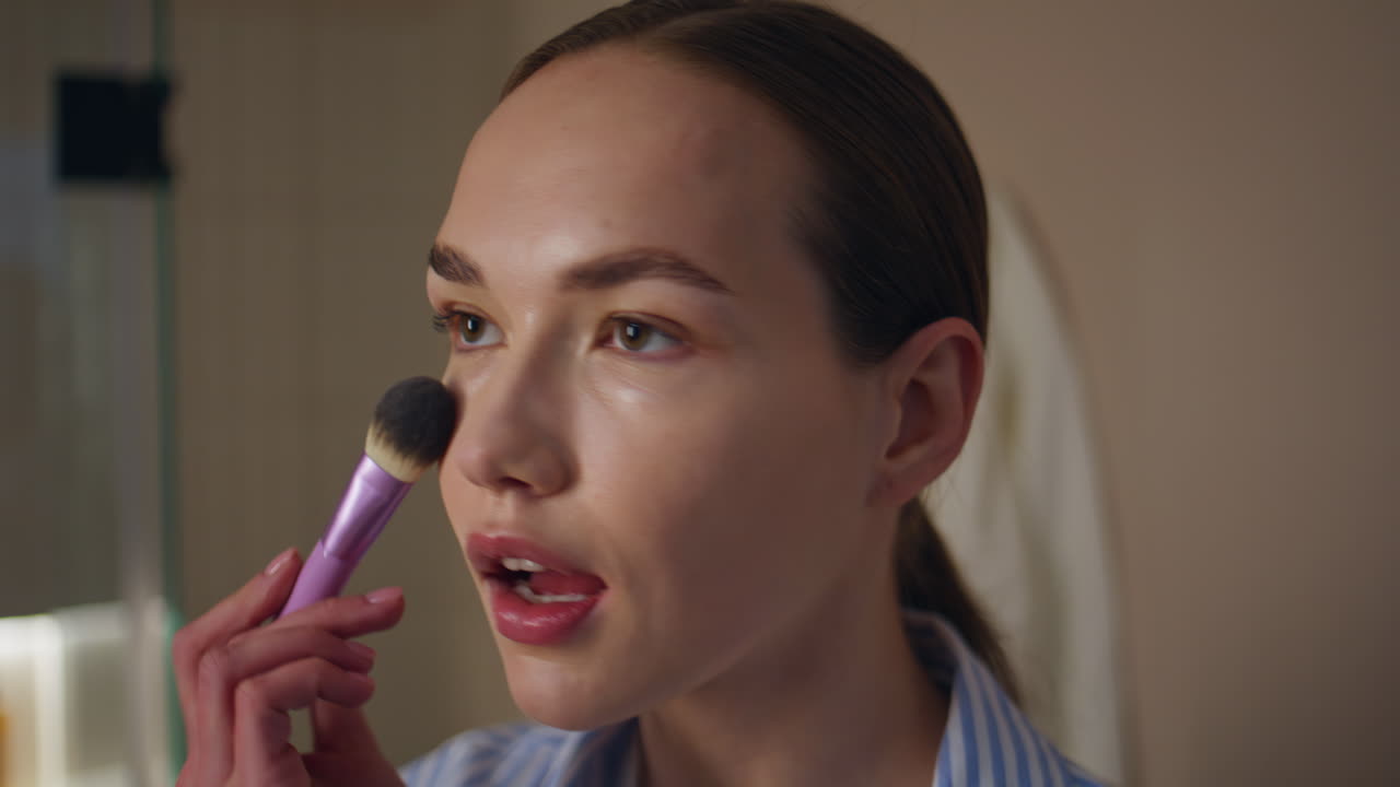 Closeup girl applying powder on face. Makeup artist do visage in evening light