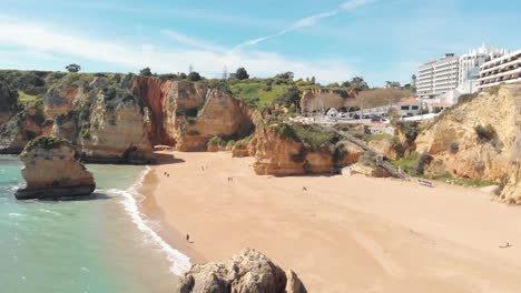 People-enjoying-majestic-shoreline-of-heavenly-Dona-Ana-beach,-Lagos,-Algarve,-Portugal---Aerial-Fly-over-Tracking-shot