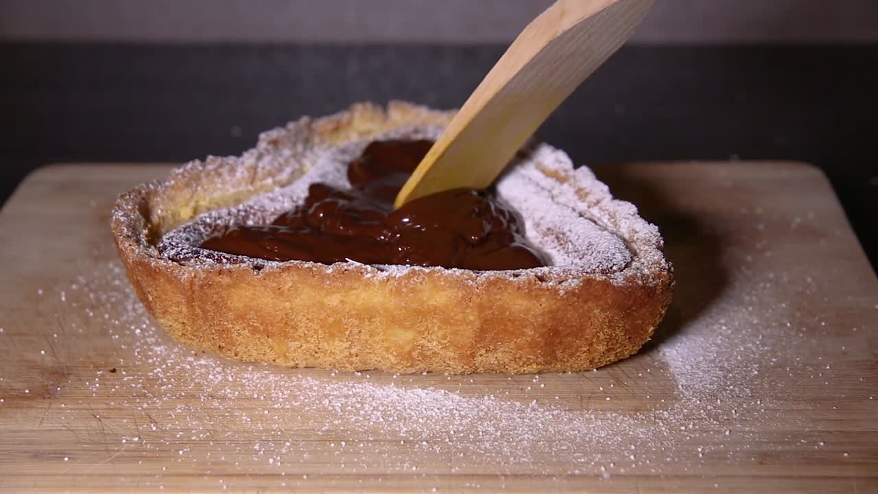 untar chocolate con una cuchara de madera en una tarta de queso en forma de corazón disparar de cerca