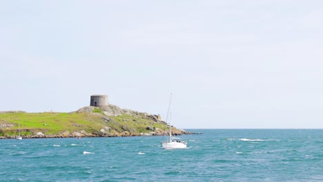 on a beautiful sunny day, dalkey island has a church ruin and a martello tower in the distance. boats are slowly coming to shore