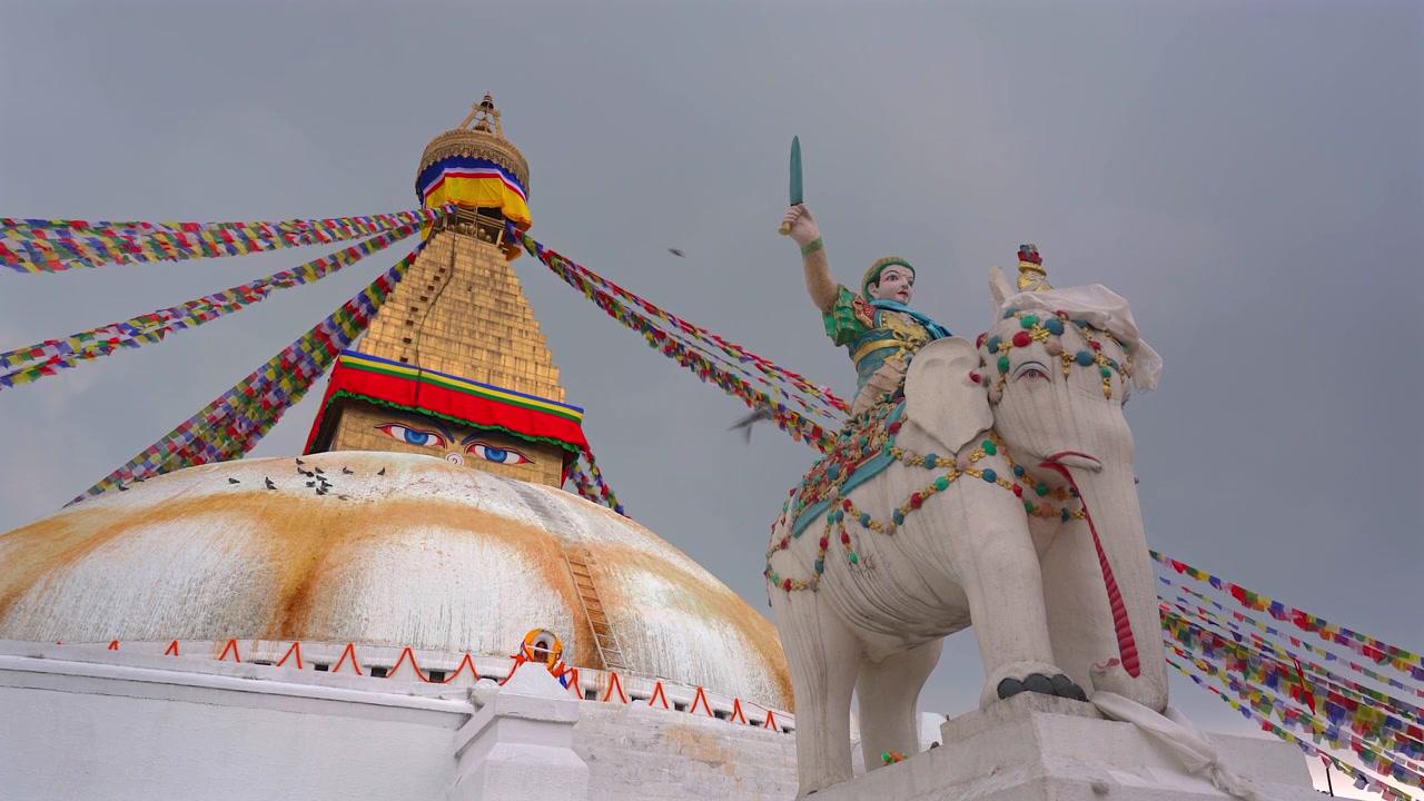 Ampia inquadratura dal basso della storica Stupa di Boudhanath accanto alla statua dell'elefante bianco che trasporta il Re Trisong Detsen contro un cielo grigio nuvoloso a Kathmandu, Nepal.