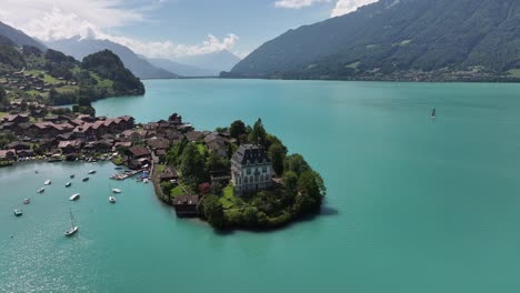 drone pulls back, iseltwald village with houses by blue lake and stunning mountains in background at lake brienz, switzerland