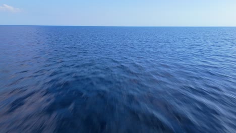 aerial pullback above calm ocean water surface texture with horizon in distance