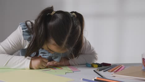 studio shot of young girl at table drawing and colouring in picture