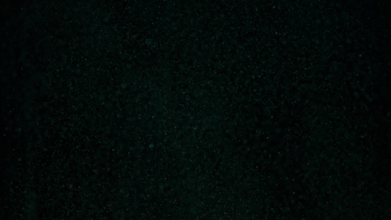 pequeñas partículas que caen en el tanque de líquido azul oscuro profundo, primer plano, cámara lenta