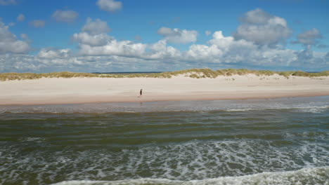 Panorama-curve-shot-of-coastal-landscape.-Man-jogging-on-sand-beach-along-sea-coast-on-sunny-day.-Denmark