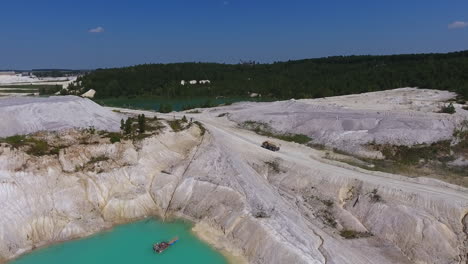loaded truck moving along the road at present day kaolin mine. white hilly ground, blue water and clear sky. green trees at the backdrop.