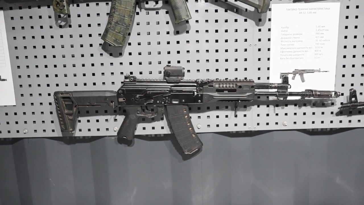 Modern assault rifle displayed on wall rack in indoor armory setting with neutral lighting