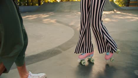 A-brunette-guy-in-a-gray-t-shirt-helps-a-girl-in-a-purple-top-and-striped-pants-ride-4-wheeled-pink-roller-skates-in-a-skate-park-on-a-concrete-floor-in-summer