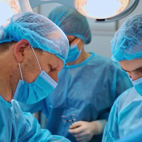 two male specialists and assistant perform a surgery. professional surgeons in blue uniform use medical instruments during an operation.