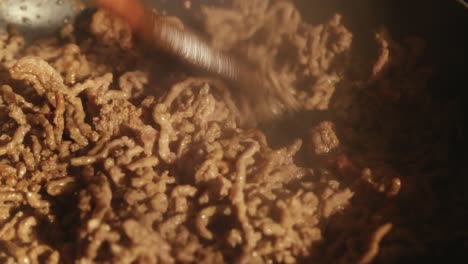 process of cooking ground meat in a pan, stirred with a wooden spatula