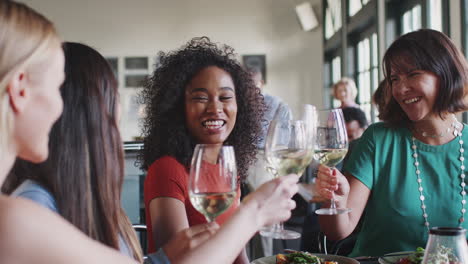 group of female friends making a toast at meal in restaurant