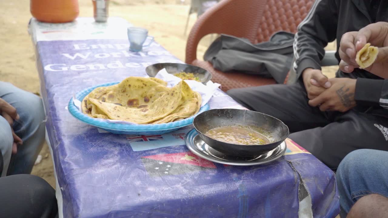 People relish a delightful breakfast at a charming local dhaba, which features warm, crispy parathas, flavorful omelets, tea, and refreshing raita.