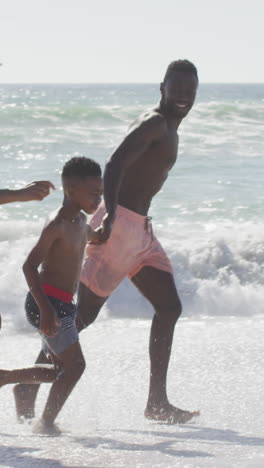 smiling african american family holding hands and running on sunny beach